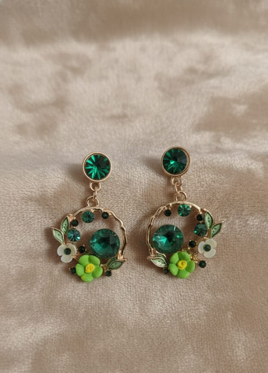 Pair of earrings with green gemstones and floral designs on a beige background