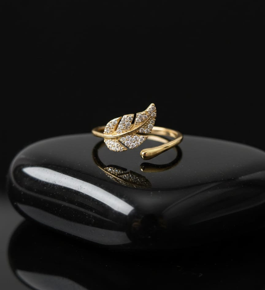 Gold and silver leaf-shaped ring on a black reflective surface