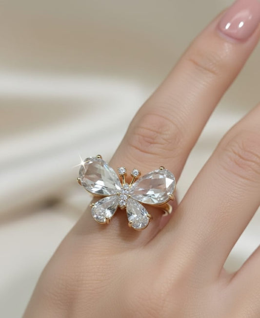 Butterfly-shaped ring with clear gemstones on a finger against a neutral background