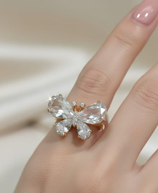 Butterfly-shaped ring with clear gemstones on a finger against a neutral background
