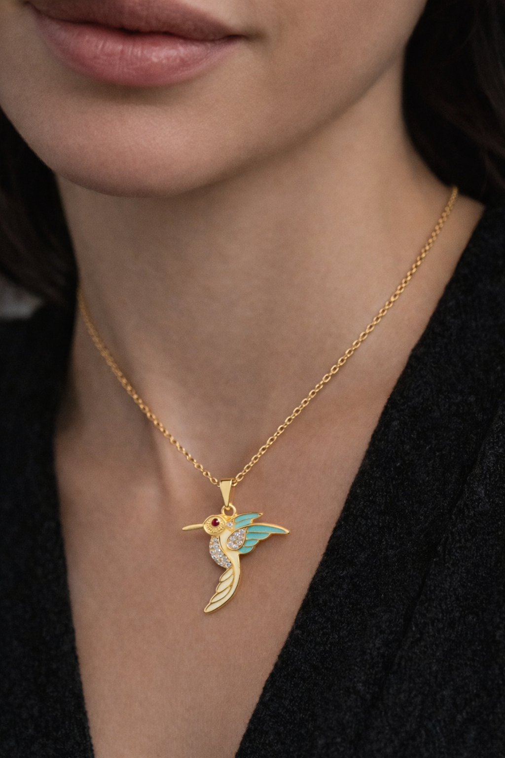 Gold necklace with a hummingbird pendant worn by a person against a dark background