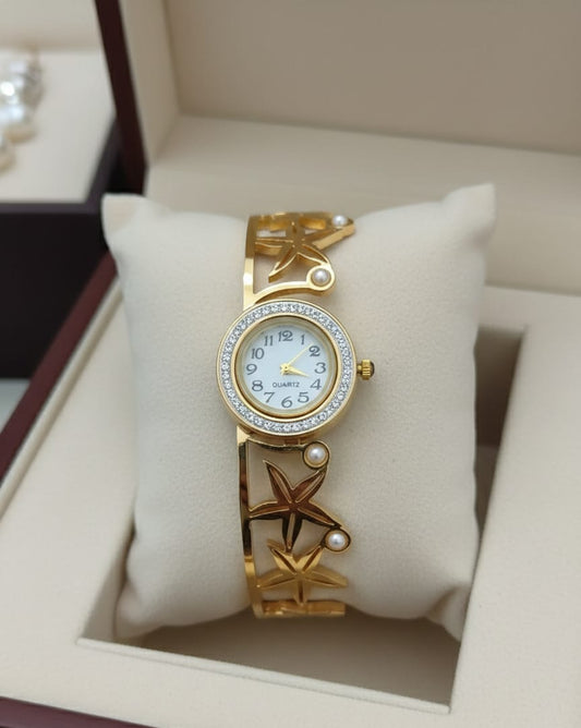 Gold wristwatch with decorative design on a white cushion in a box