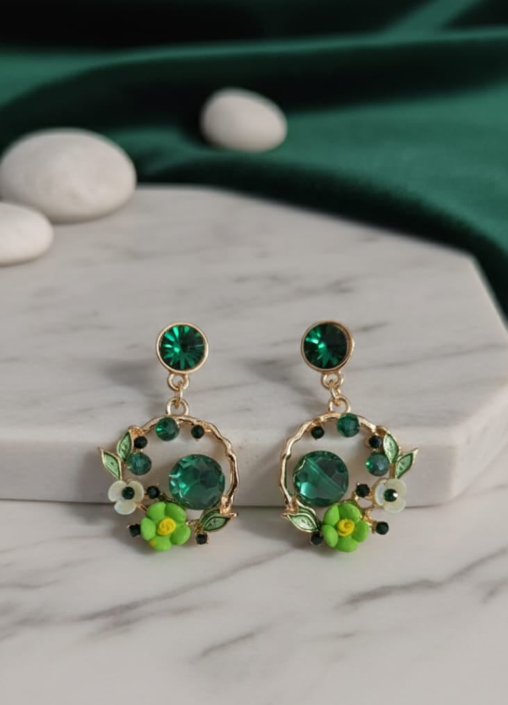 Green gemstone earrings on a marble surface with a green fabric background