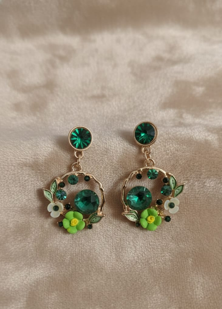 Pair of earrings with green gemstones and floral designs on a beige background