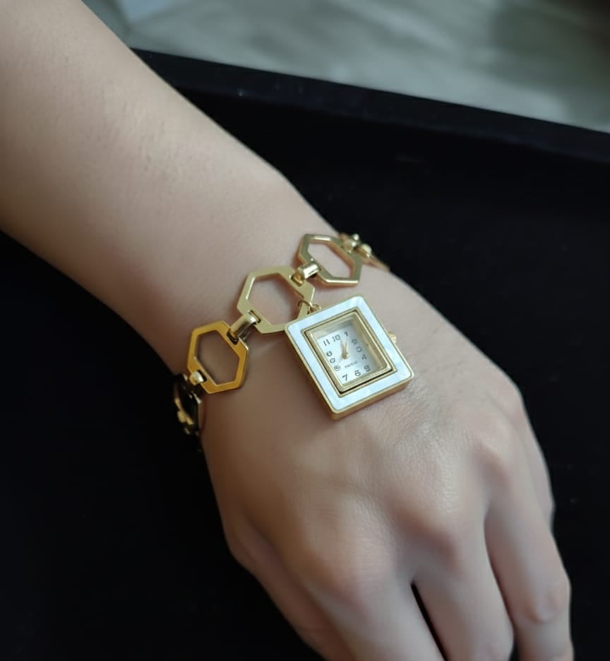 Gold bracelet with a square charm on a wrist against a dark background