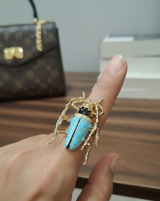 Gold and turquoise beetle-shaped ring on a finger with a blurred background