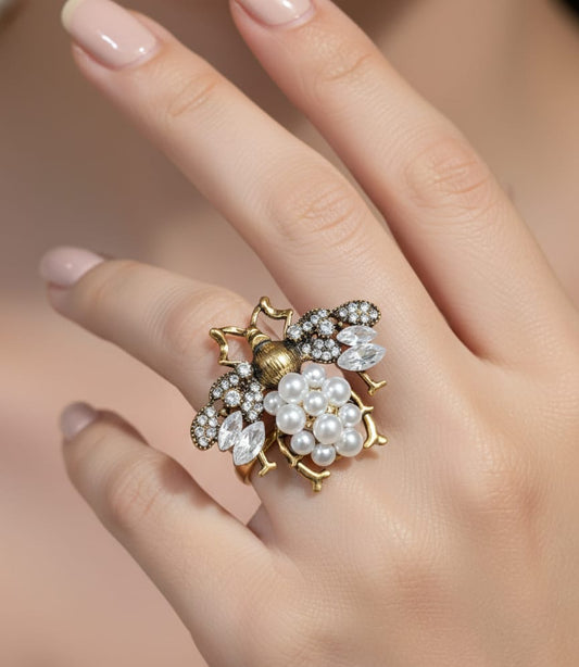 Close-up of a hand wearing an ornate ring with pearls and gemstones on a neutral background