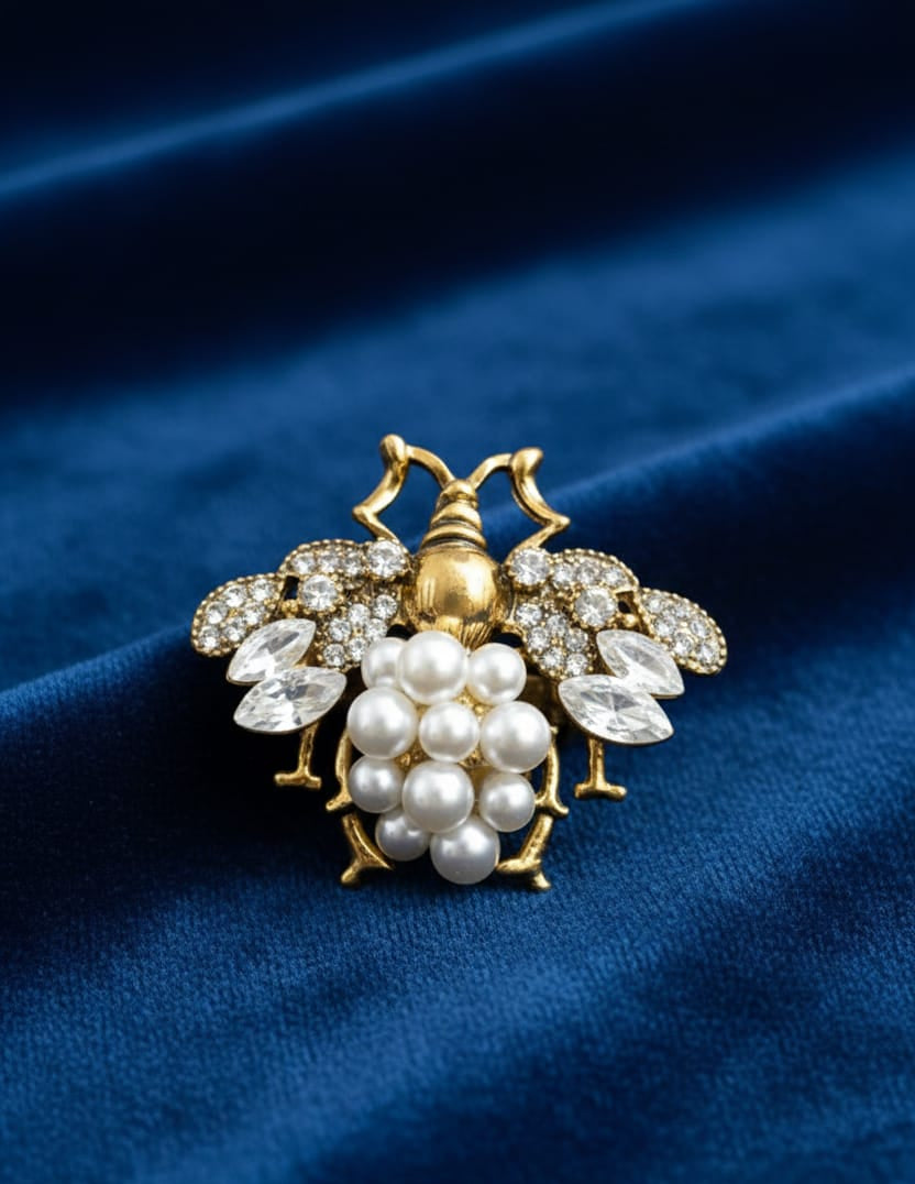 Gold bee-shaped brooch with pearl cluster on a blue fabric background